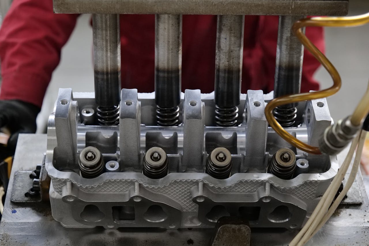 about-02 Detailed view of a metallic engine cylinder head with springs and pistons, assembled in an industrial workshop.
